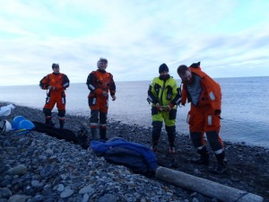 Nils, Ted og Tom Richard skifter om til kystvaktas overlevingsdrakter og er klar for hjemreise. Stasjonssjef Kåre bivåner det hele og transporterer dem ut til KV Svalbard.